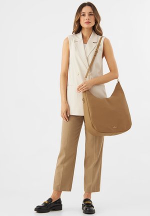 Ruskean nahkainen olkalaukku, jossa on pehmeä, kaareva muoto ja kultainen logovihje. Mallilla on päällään beige räätälöity asu ja mustat loaferit.