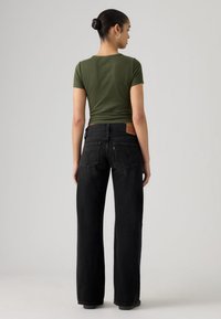 Μαύρα τζιν με φαρδύ πόδι και ψηλή μέση, κατασκευασμένα από ντένιμ, με πίσω τσέπες και δερμάτινο διακοσμητικό. Συνδυάζονται με πράσινο εφαρμοστό μπλουζάκι.