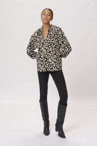 Blusa leopardata nera e beige con scollatura a V, maniche plissettate e vestibilità morbida. Abbinata a jeans skinny neri e stivali neri fino al ginocchio.