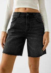 Pantalones cortos de mezclilla negra con corte recto, dobladillo deshilachado, diseño de cinco bolsillos y cierre de botón. Material texturizado, ajuste informal.