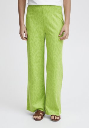 Pantalons larges verts avec un motif léopard subtil, fabriqués dans un tissu doux. Associés à des sandales marron.