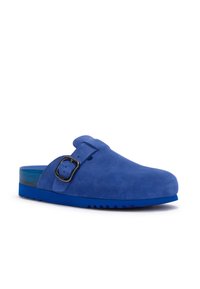 Scarpa slip-on in suede blu con cinturino regolabile nero e suola testurizzata, mostrata su uno sfondo bianco.