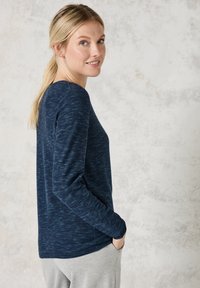 Marinefarbendes Langarmshirt mit strukturiertem, gestreiftem Design, ausgestattet mit Rundhalsausschnitt und leicht lockerer Passform. Trägt dazu eine hellgraue Hose.