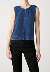 Haut sans manches en denim bleu avec un col rond, un détail de couture à l'avant et une coupe courte, associé à un jean noir. Texture lisse.