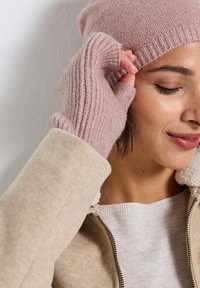 Ljusrosa stickad mössa och fingervantar i mjukt ullblandning. Vantarna har ribbat mönster. Bärs med en beige fleecefodrad jacka.
