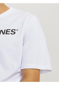 Hvid bomulds T-shirt med korte ærmer og rund halsudskæring, med fed sort tekst på forsiden og en glat, blød tekstur.