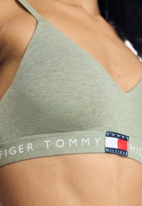 Olívazöld bralette V-nyakú kivitelben, textúrált anyaggal, és egy fehér szalagnál a "TOMMY HILFIGER" felirattal és logó foltokkal.