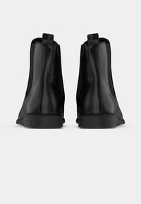 Schwarze Leder-Chelsea-Boots mit glatter Oberfläche, runder Zehenpartie, elastischen Seitenpaneelen und niedrigem, gestapeltem Absatz.