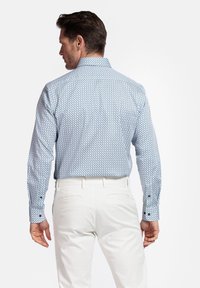 Chemise bleu clair à manches longues avec un motif géométrique, poignets boutonnés et col, associée à un pantalon blanc. Fini textile lisse.