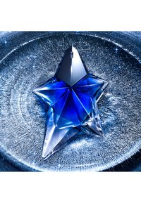 Botella de perfume azul en forma de estrella con base transparente y detalles metálicos, reflejando la luz sobre un fondo texturizado de purpurina.