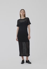 Abito nero in pizzo con un motivo a zigzag testurizzato, caratterizzato da maniche corte e un design aderente di lunghezza media. Indossato sopra un intimo a tinta unita.