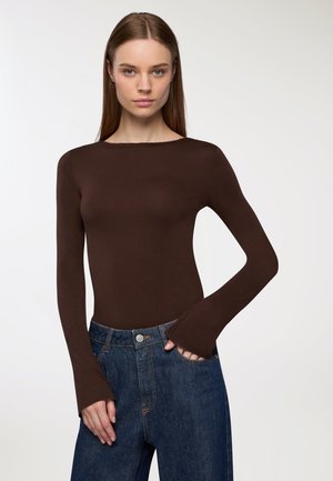 Maglia marrone a maniche lunghe con scollo a barca e polsini svasati, abbinata a jeans in denim blu a vita alta. Tessuto dal tocco morbido.