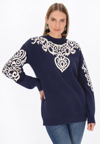 Donkerblauwe sweater met crèmekleurige borduursels met bloemen- en hartpatronen rondom de halslijn en op de mouwen. Ribgebreide boorden en onderrand.