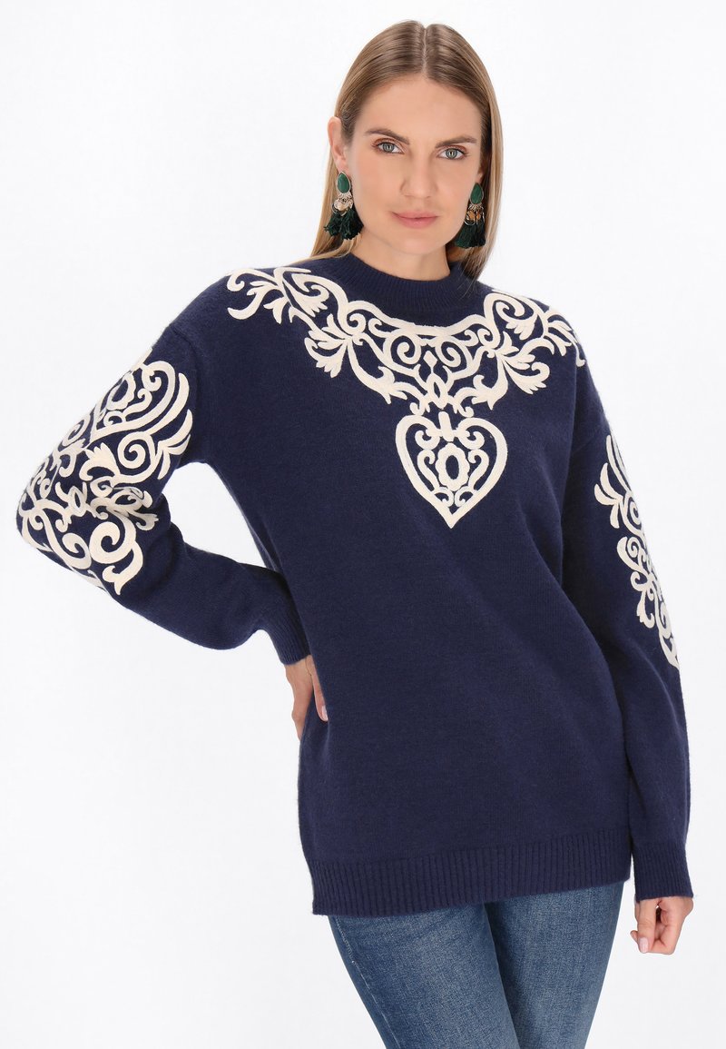 Donkerblauwe sweater met crèmekleurige borduursels met bloemen- en hartpatronen rondom de halslijn en op de mouwen. Ribgebreide boorden en onderrand.