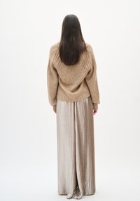 Beżowy sweter dzianinowy o luźnym kroju, w połączeniu z długą, plisowaną srebrną spódnicą wykonaną z błyszczącego, gładkiego materiału.