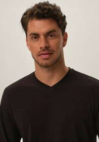 Czarna, długosleeve koszulka w serek, wykonana z miękkiej tkaniny, cechująca się gładką teksturą i dopasowanym krojem, noszona przez mężczyznę o jasnej karnacji.