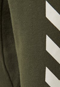 Olivgrön tyg med en slät textur, som har ett vitt zigzagmönster på ena sidan. Materialet verkar mjukt och något stretchigt.