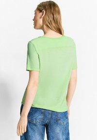 Lys grøn kortærmet t-shirt lavet af et blødt, tekstureret stof, med rund halsudskæring og en afslappet pasform, parret med blå jeans.