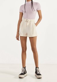 Světlofialový přiléhavý top s krátkými rukávy a vroubkovaným výstřihem, doplněný o krémové šortky s vysokým pasem, páskem a kapsami.