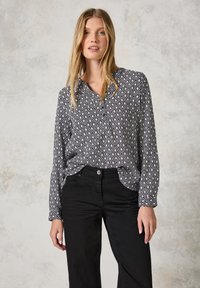 Långärmad blus i svart och vitt geometriskt mönster, med krage och knapp fram, tillsammans med svarta byxor.