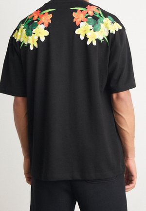 Man wearing black short-sleeve shirt with orange and yellow floral patterns across the upper back and shoulders.