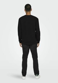 Zwarte sweatshirt met lange mouwen en geribbelde boorden, gecombineerd met donkere jeans. Heeft een klassieke ronde halslijn en een ontspannen pasvorm. Witte sneakers.