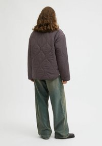 Veste matelassée surdimensionnée en gris foncé, avec un ourlet arrondi et des manches larges. Associée à un jean ample de couleur vert pâle et des chaussures noires.