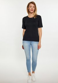 Černé tričko s krátkým rukávem a kulatým výstřihem, zkombinované s světle modrými skinny džíny a bílými teniskami na neutrálním pozadí.