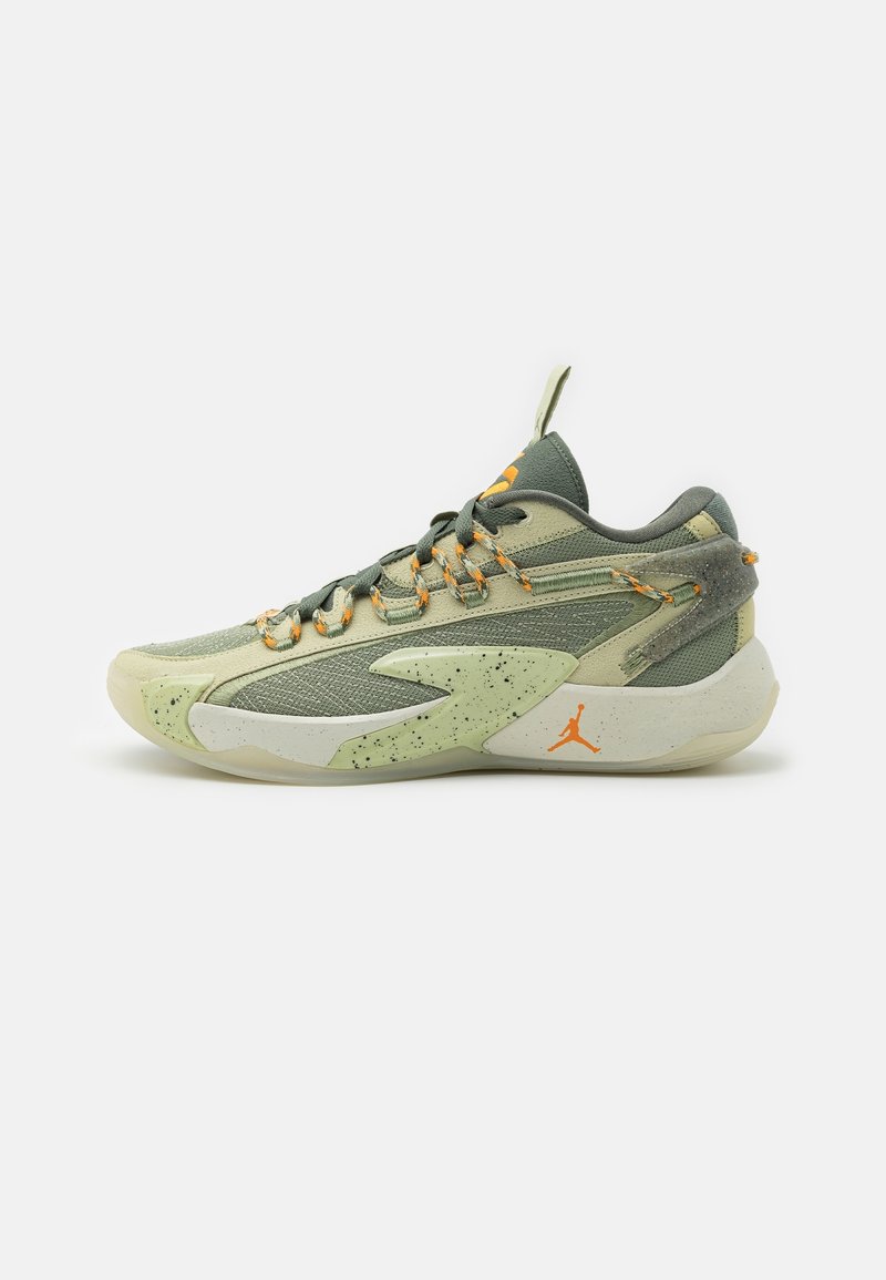 Chaussure de sport basse en vert et beige avec des accents orange, semelle intermédiaire mouchetée, textures en mesh et daim, et une languette avec une tirette.