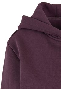 Gros plan d'un sweat à capuche violet plié montrant la couture de l'épaule et de la capuche avec une texture de tissu en coton doux.