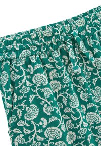 Pantalons floraux turquoise avec taille élastique, présentant un motif floral blanc et un tissu texturé. Aucune poche visible en gros plan.