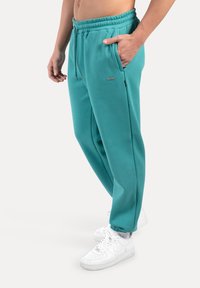 Turkosa joggingbyxor med elastisk midja och sidofickor. Mjukt material med lös passform, kombinerat med vita sneakers.