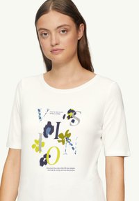 T-shirt blanc à manches courtes avec des graphismes floraux colorés et le texte "VISION". Matière en coton doux avec un col rond.