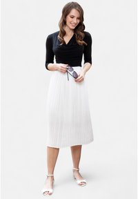 Musthave mustemel sõlgadega must pikkade varrukatega topp, millel on langev kaelus, kombineeritud pleediribadega valge midi seeliku. Modell hoiab musti päikeseprille ja kannab valgeid sandaale.