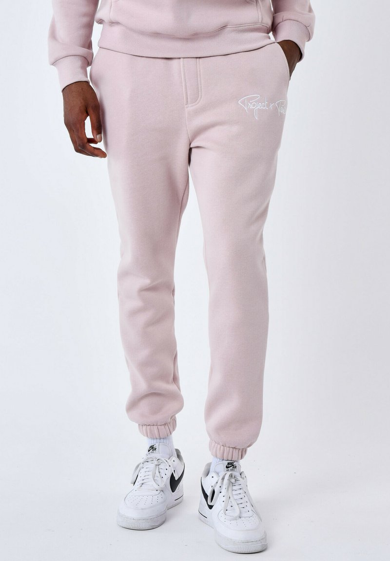 Pantalones jogger rosa claro hechos de tela suave con cintura y puños elásticos. Presenta un logo en script blanco en la cadera izquierda.
