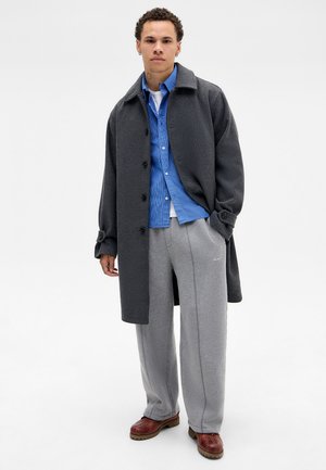 Gray wool coat over a blue checkered shirt, paired with gray sweatpants and brown leather shoes. Black buttons and a collar detail visible.