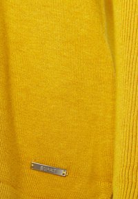 Gul stickad tröja med texturerad tyg, ribbade kanter och en silverfärgad "Esprit" logotyp tagg vid fållen.