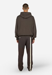 Ciemnoszara bluza z kapturem, z kieszenią typu kangur i ściągaczami przy mankietach. Pasujące spodnie mają boczny biały pasek oraz gradient od ciemnoszarego do jasnoszarego.