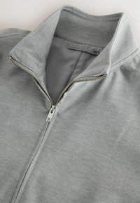 Gray zip-up jacket featuring a high collar, smooth texture, and silver zipper detail. The fabric appears soft and casual.