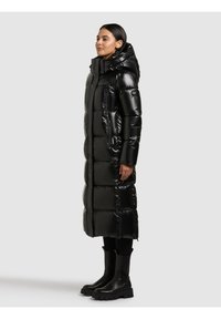 Melna pūkota virsjaka ar spīdīgu apdari, lielām šūtām daļām, augstu apkakli un kabatām ar rāvējslēdzējiem. Kombinēta ar masīvām melnām zābakiem.