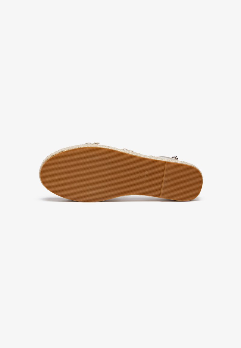 Suela de zapato de goma con una superficie texturizada de color marrón claro, que presenta ranuras horizontales y una forma curva sin detalles adicionales.