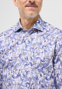 Blomstret button-up skjorte i blå og hvid med mønster af blade og blomster, en klassisk krave og glat stofstruktur.
