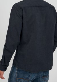 Camisa de manga larga azul oscuro hecha de tela texturizada, con dobladillo recto, puños con botones y cuello clásico. Usada con jeans de mezclilla.