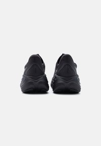 Ζεύγος μαύρων αθλητικών παπουτσιών με χοντρές σόλες, εμφανιζόμενα από πίσω, με υφασμένες ενισχύσεις στη φτέρνα και την επωνυμία «Skyward».