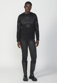 Maglione nero lavorato a maglia con un motivo floreale testurizzato, abbinato a jeans skinny scuri e stivali neri al ginocchio. Design semplice e monocromatico.