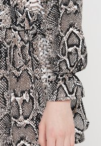 Abito a stampa serpente nero e beige con un design testurizzato. Presenta maniche a sbuffo e dettagli fru-fru ai polsini.