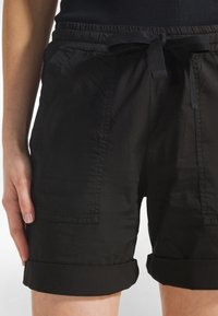 Schwarze Shorts aus leichtem Stoff mit einem elastischen Bund, gebunden mit einem Stoffgürtel, mit umgeschlagenen Säumen und Seitentaschen.