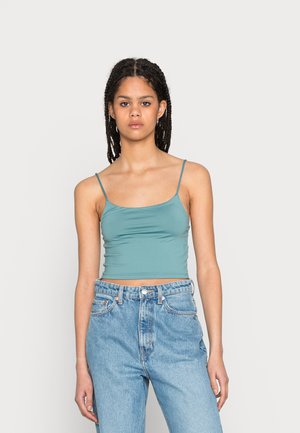 Top cropped em tom verde-água com alças finas, textura suave e design ajustado. Combinado com jeans de ganga de cintura alta em azul claro.