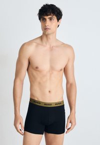 Schwarze Boxershorts mit einem goldenen "HUGO"-Bund. Weicher, dehnbarer Stoff in enganliegendem Design, mit mittelhohem Schnitt und flachen Nähten.