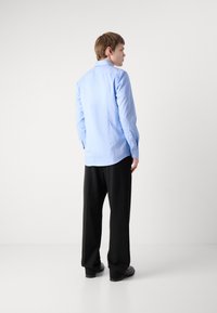 Camisa de manga larga azul claro, con puños abotonados, de corte recto, combinada con pantalones negros holgados. Textura de tela suave sin patrones visibles.